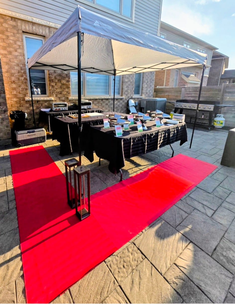 Backyard live pizza setup with a tent, red carpet and prep tables on a residential patio