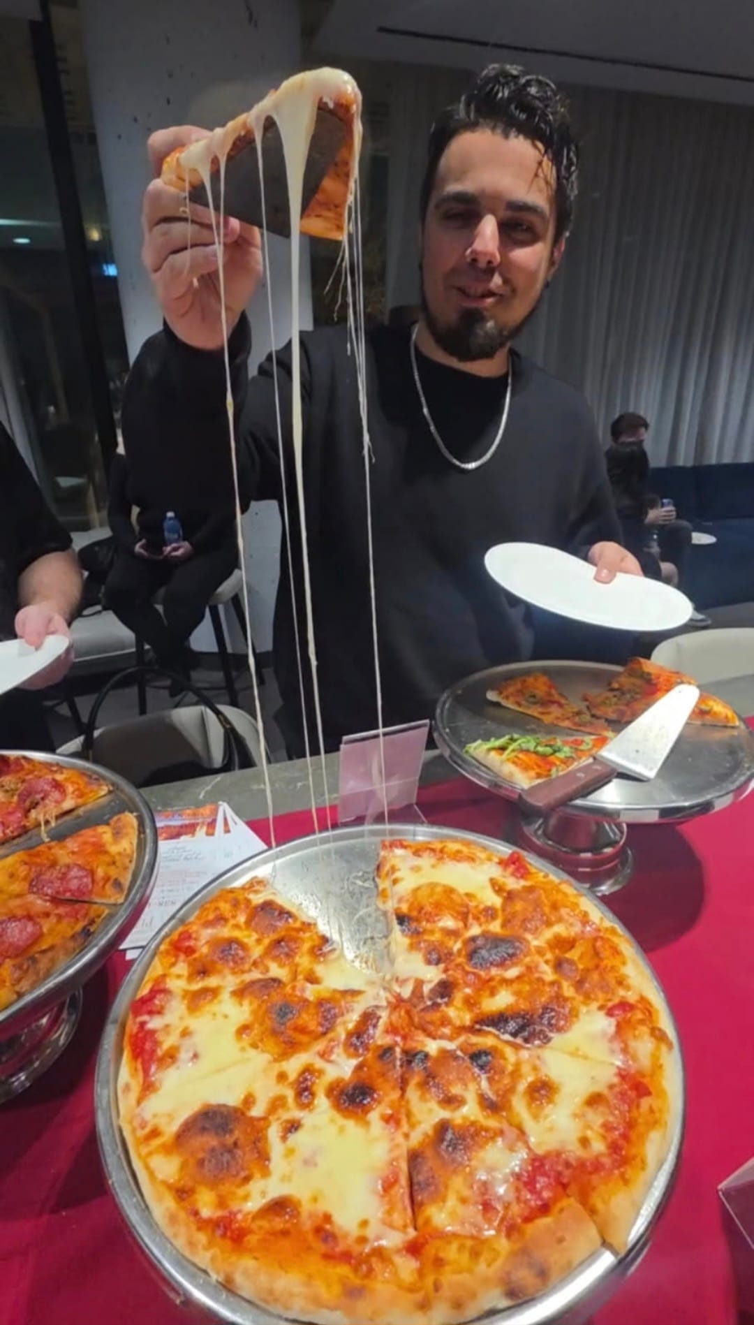 Long stretchy cheese pull from a fresh stone-baked pizza slice at an upscale evening event
