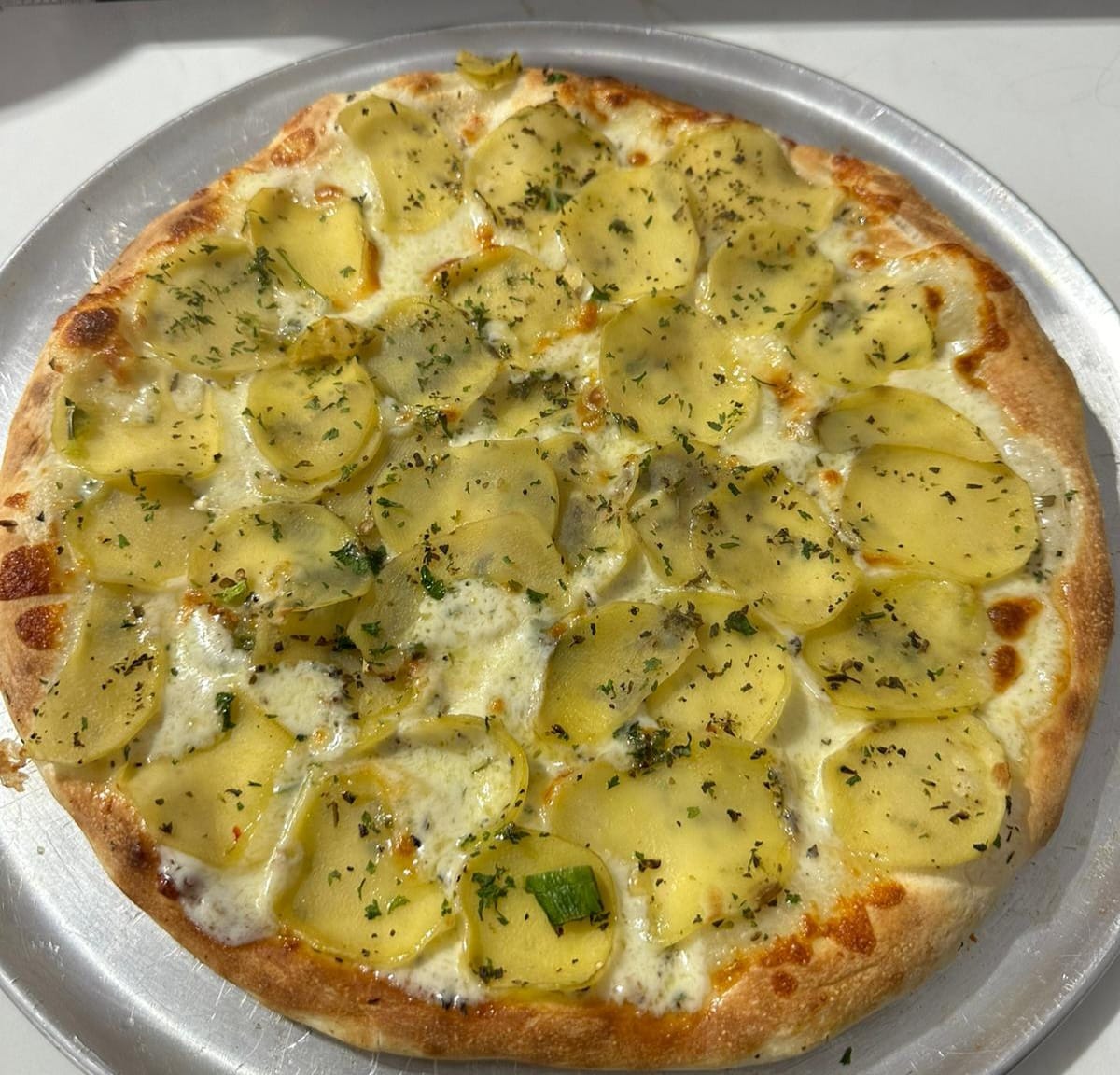 Stone-baked white pizza topped with thinly sliced potato, herbs and melted cheese