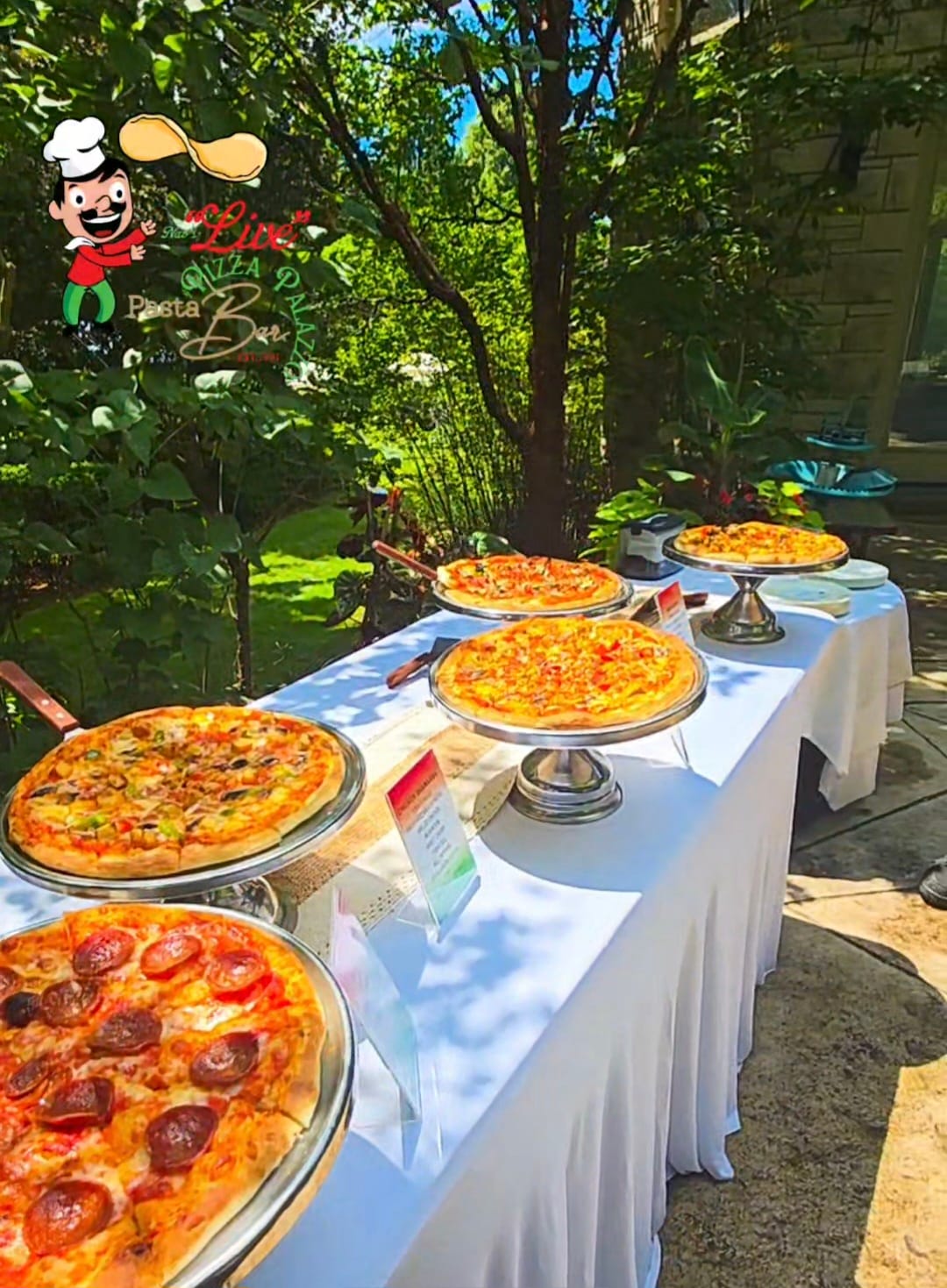 Outdoor live pizza display on a white-linen table in a garden setting