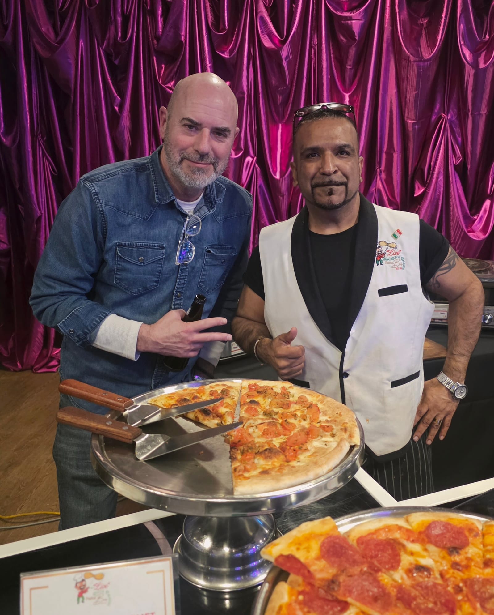 Nav posing with a guest beside a fresh pizza at a celebration