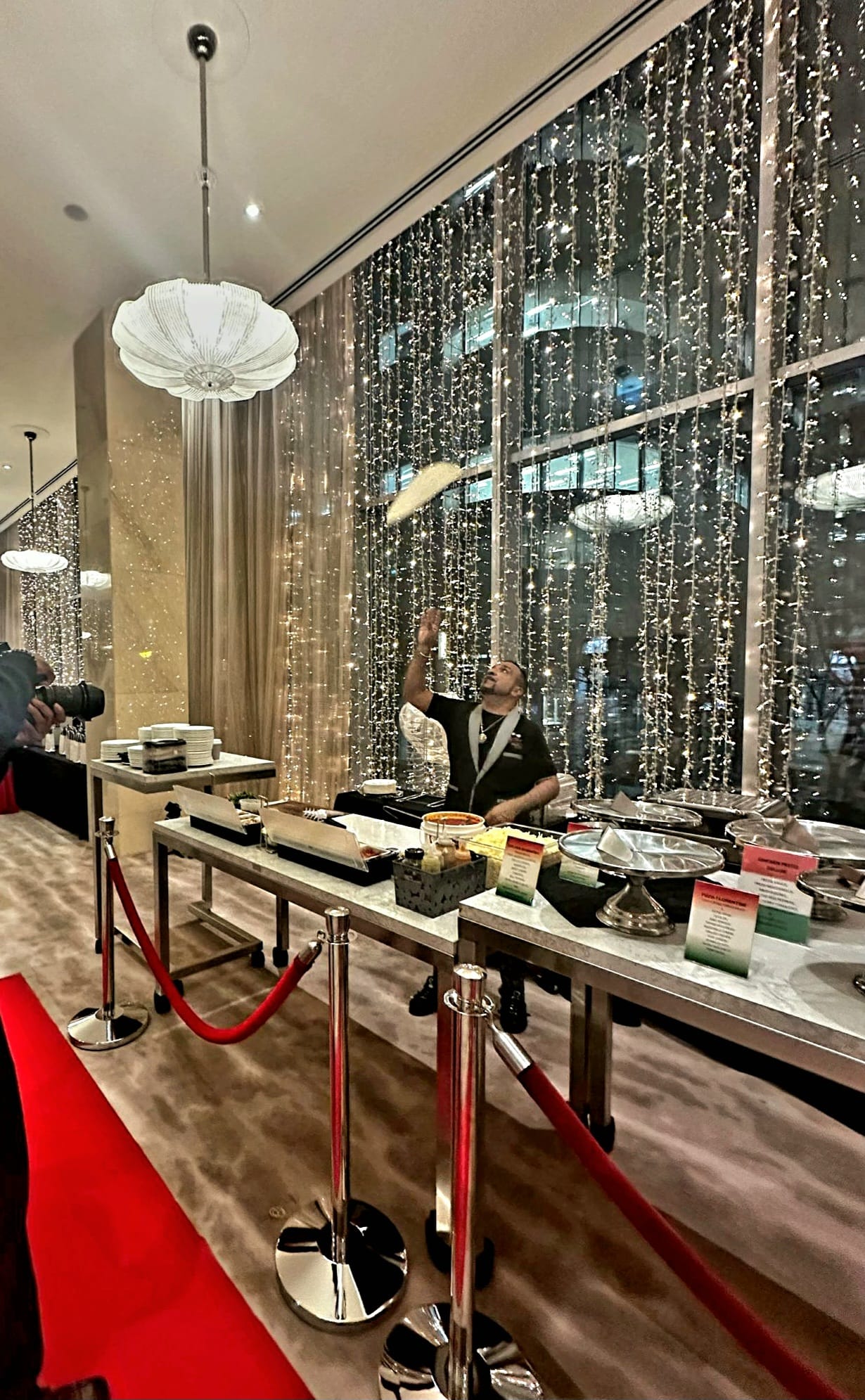 Nav tossing pizza dough high in the air in front of the sparkling fairy-light window at the Ritz-Carlton Toronto